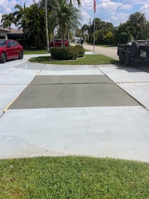 Freshly poured, dark grey concrete patch in the middle of a lighter grey residential driveway on a sunny day.