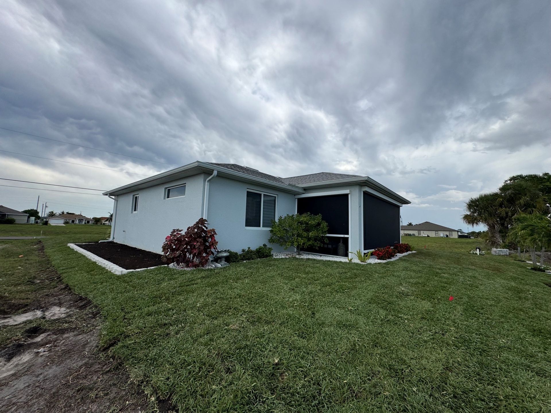 Small white house with a gray roof on a grassy lot under a cloudy sky