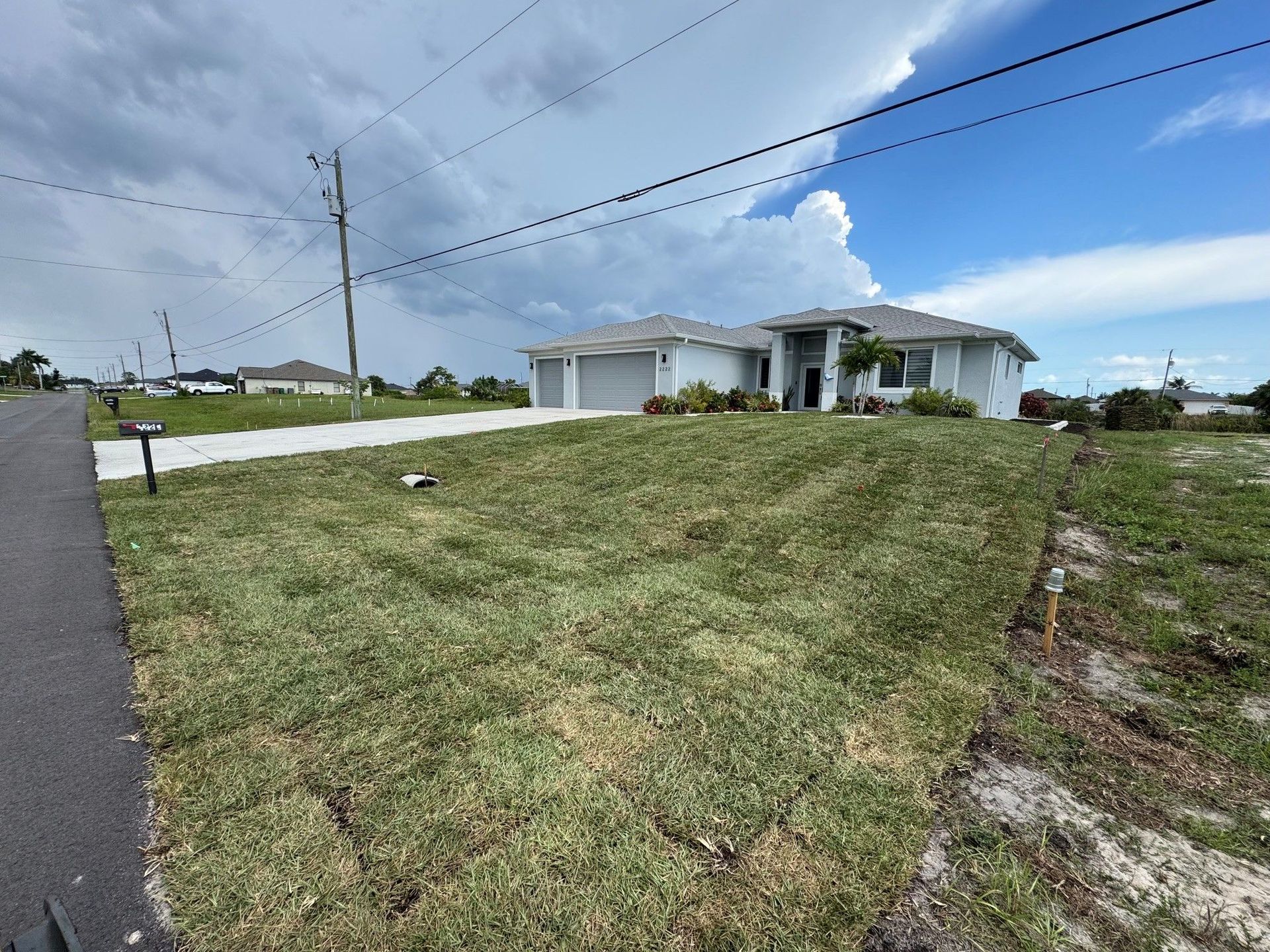 Suburban house with white exterior, driveway, and large grassy front yard under a partly cloudy sky