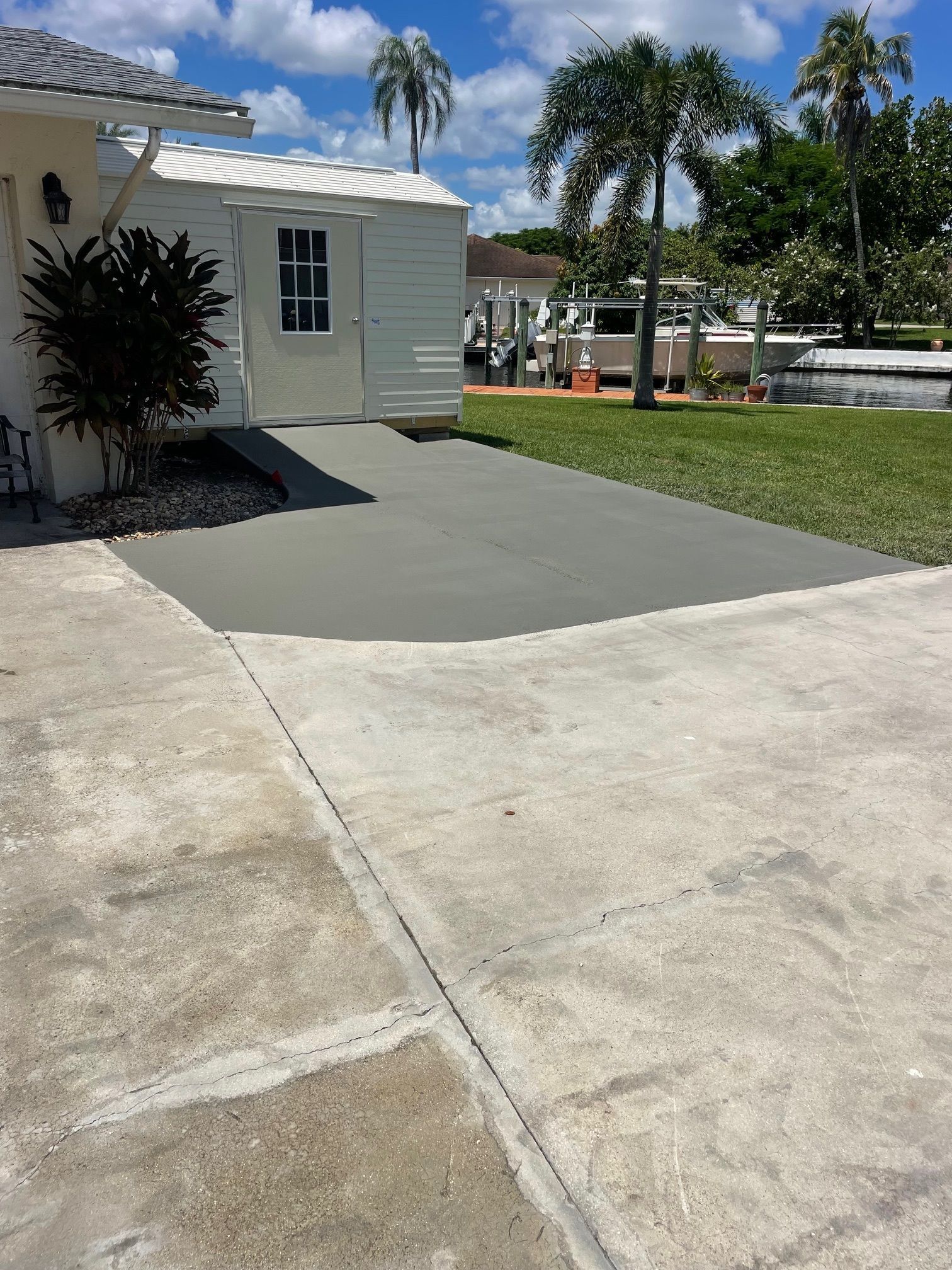 Concrete driveway with a newly poured gray section next to a white building, with palm trees and grass visible.