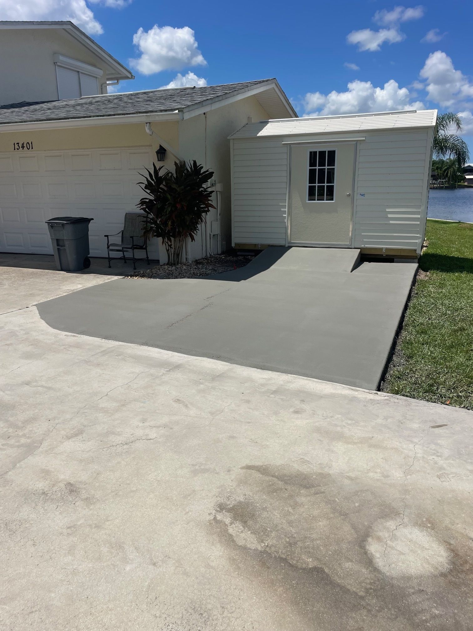 A concrete ramp leads to a white shed next to a yellow house.  The scene is outdoors in bright sunlight.