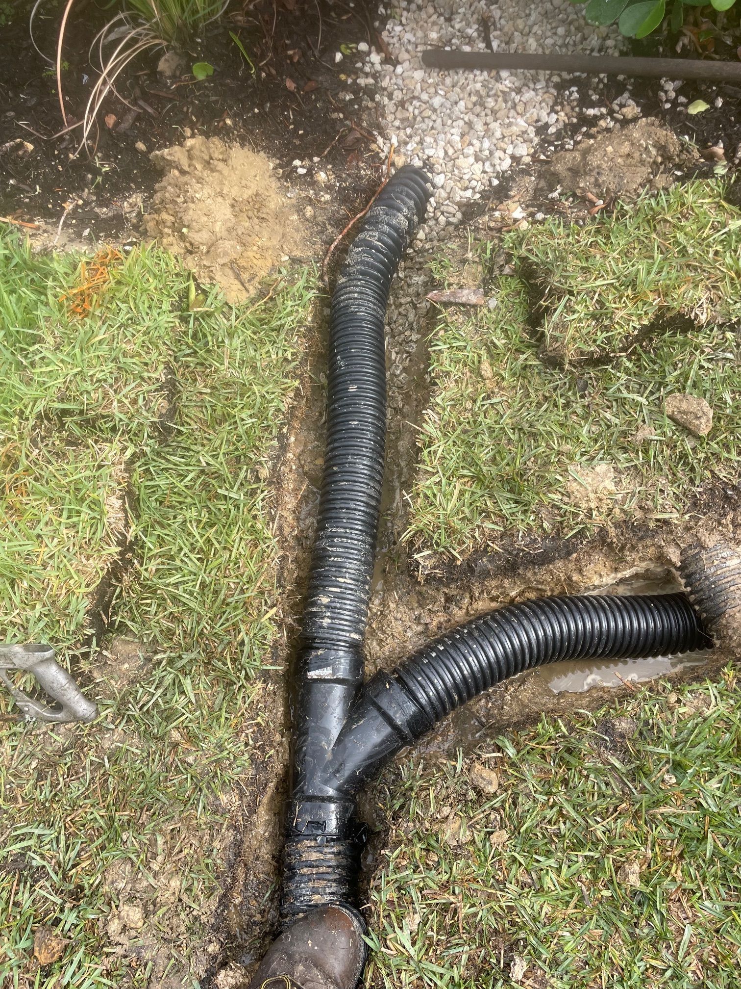 Black corrugated drain pipe in a trench, connected with a Y-fitting.