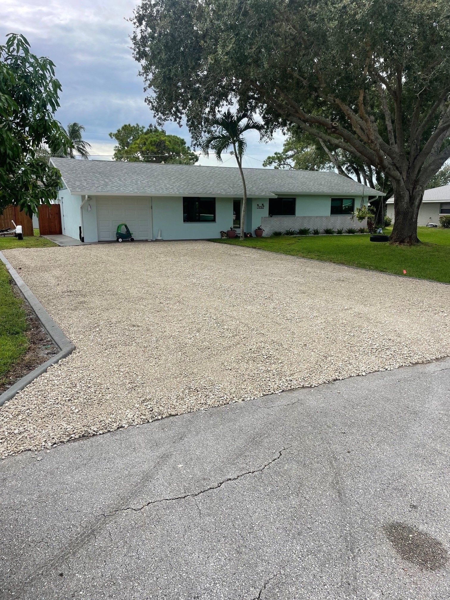 Single-story white house with a gravel driveway and large trees in front