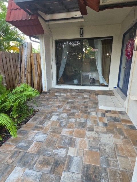 A patio with multi-toned, rectangular pavers leading to a glass sliding door and a blue entry door.