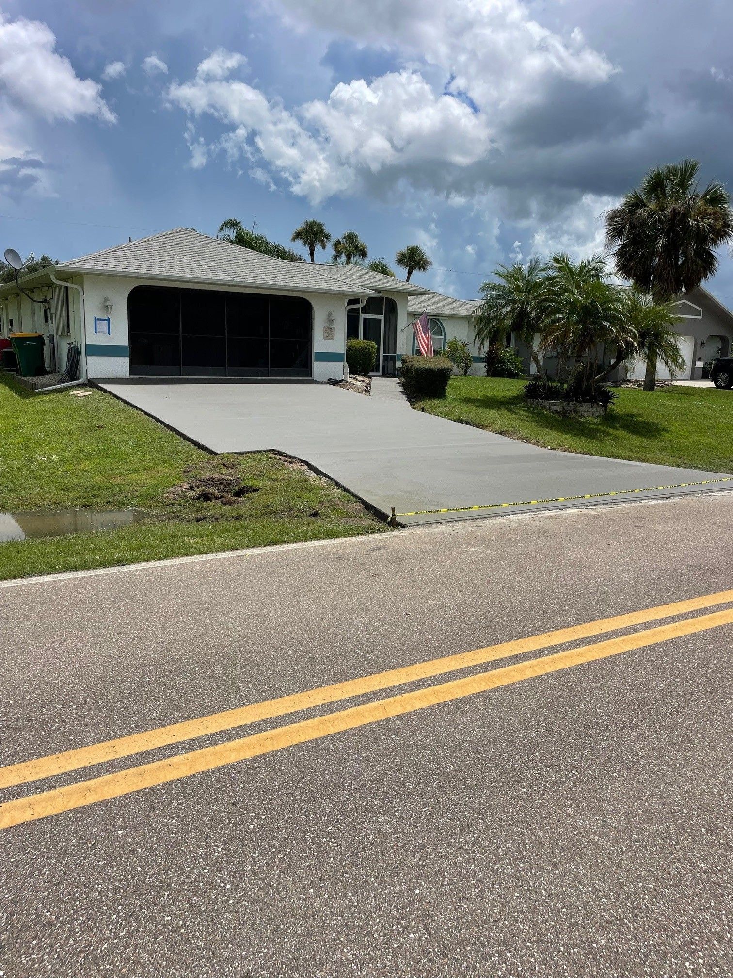 Suburban house with a wide driveway, double garage, palm trees, and a partly cloudy sky.
