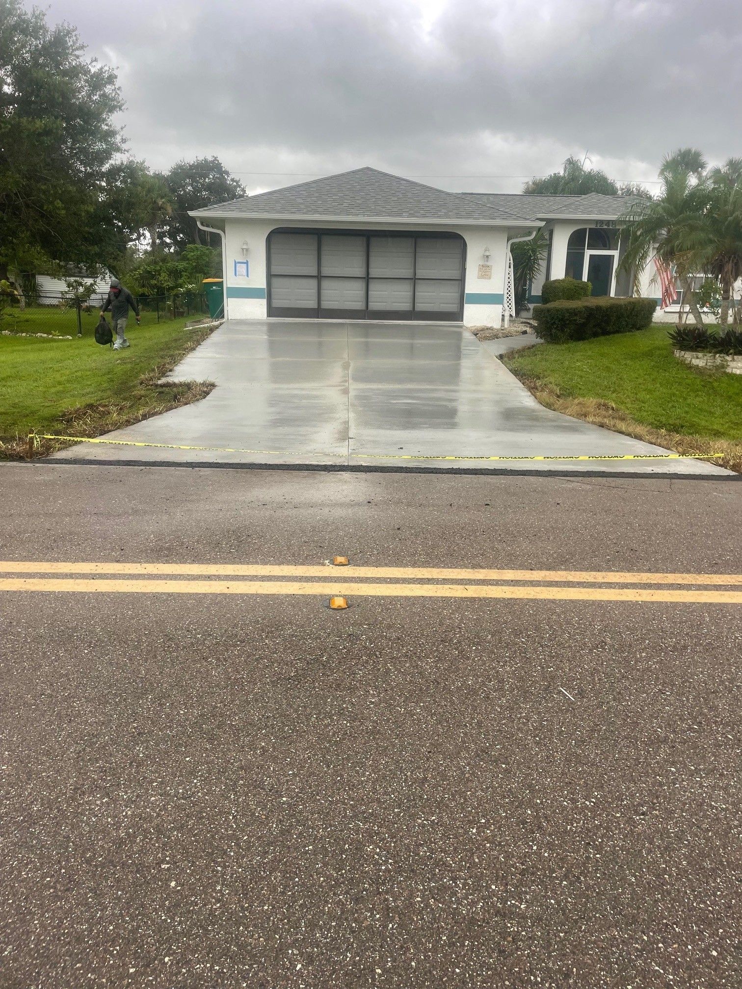 Single-story house with a gray garage door and wet driveway on a rainy street.