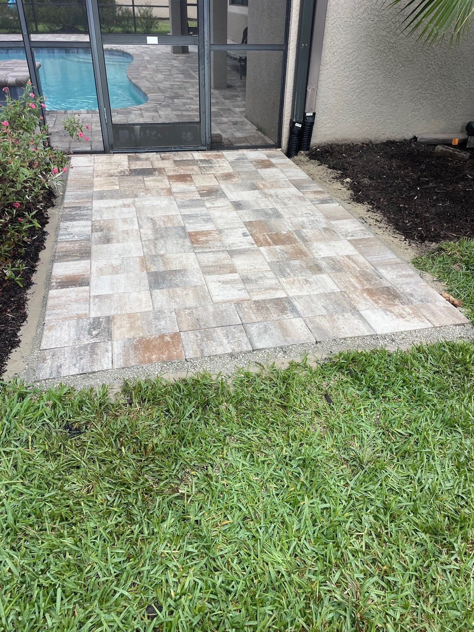 Stone patio beside a grassy lawn near a screened pool enclosure and house wall