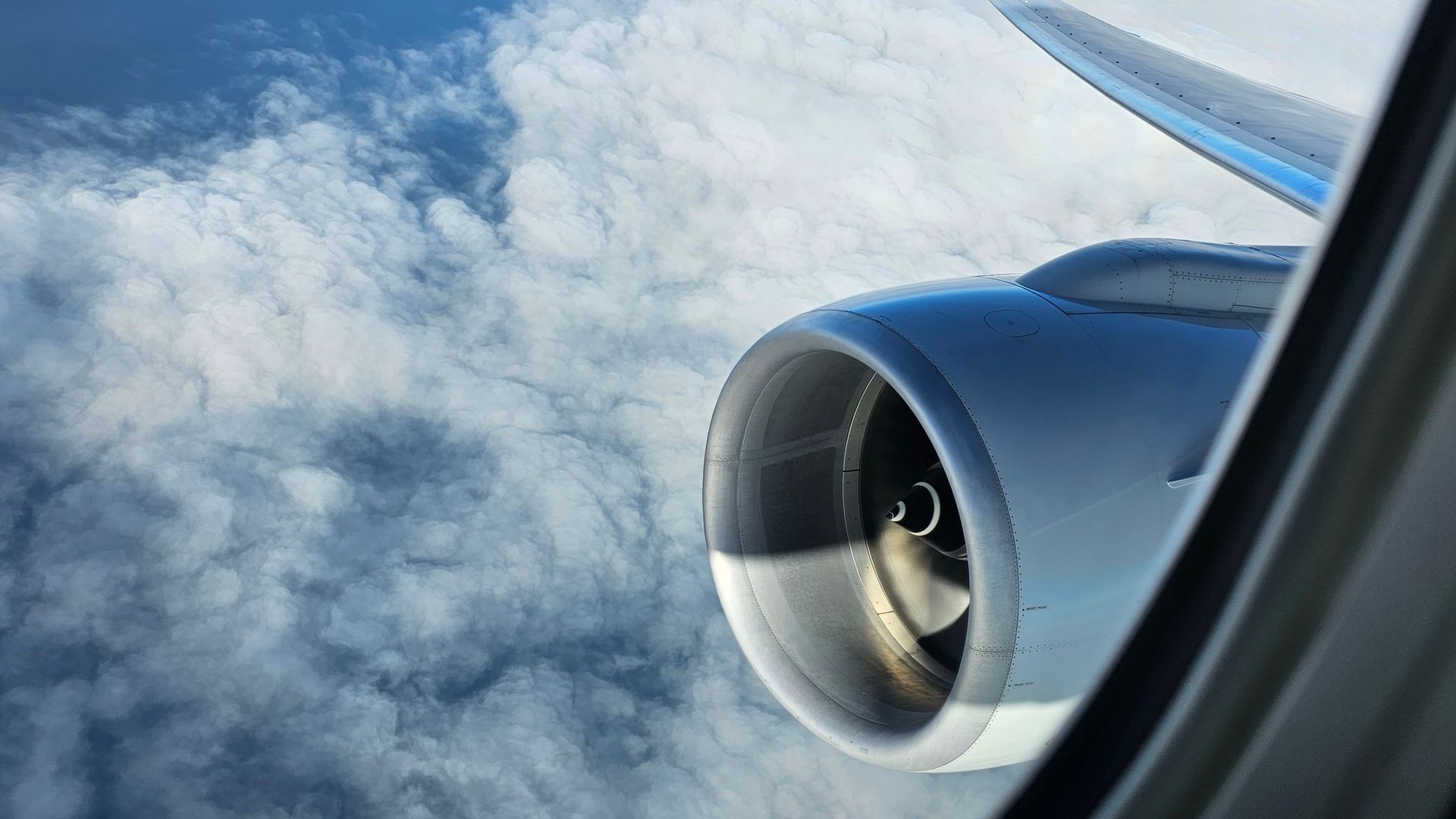 View from an airplane window showing a close-up of the aircraft engine and wing above a blanket of soft, white clouds—symbolizing flight, travel, and the spirit of aviation.