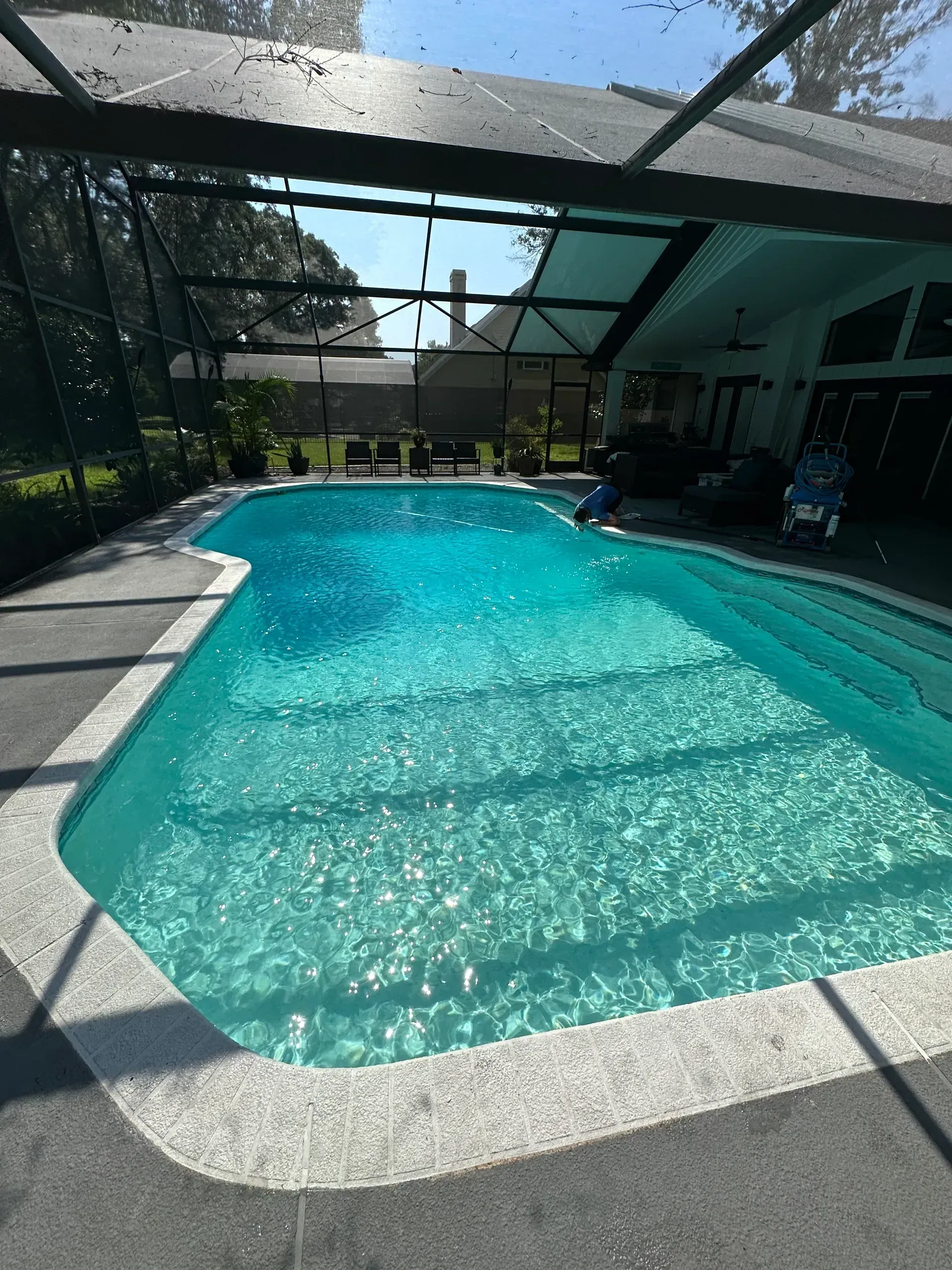 A large swimming pool is surrounded by a screened in area.