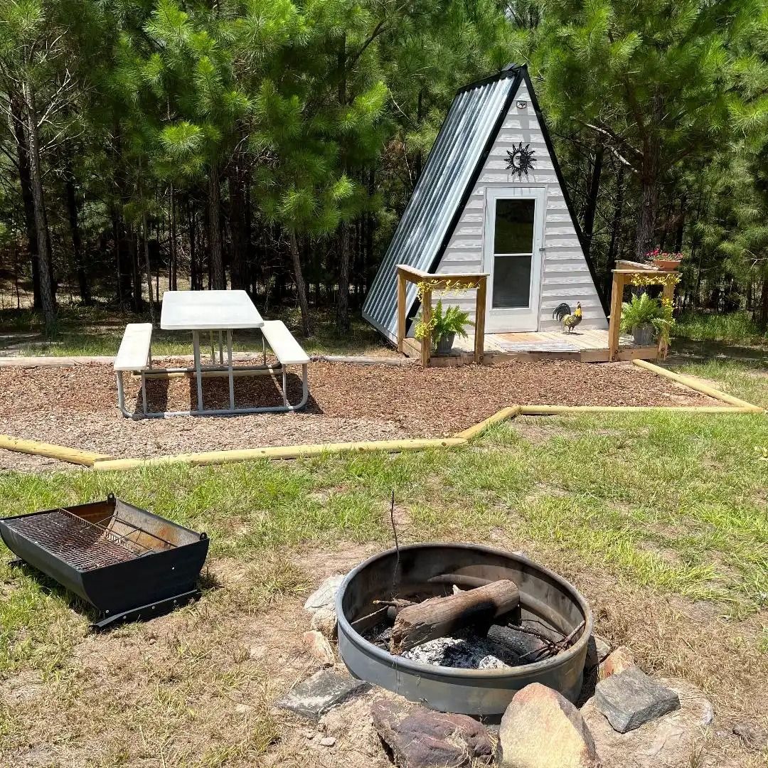 A-frame cabin in a wooded campsite with picnic table and fire pit