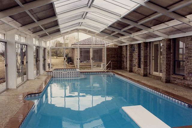 Indoor swimming pool with blue water under a glass roof in a brick-walled enclosure