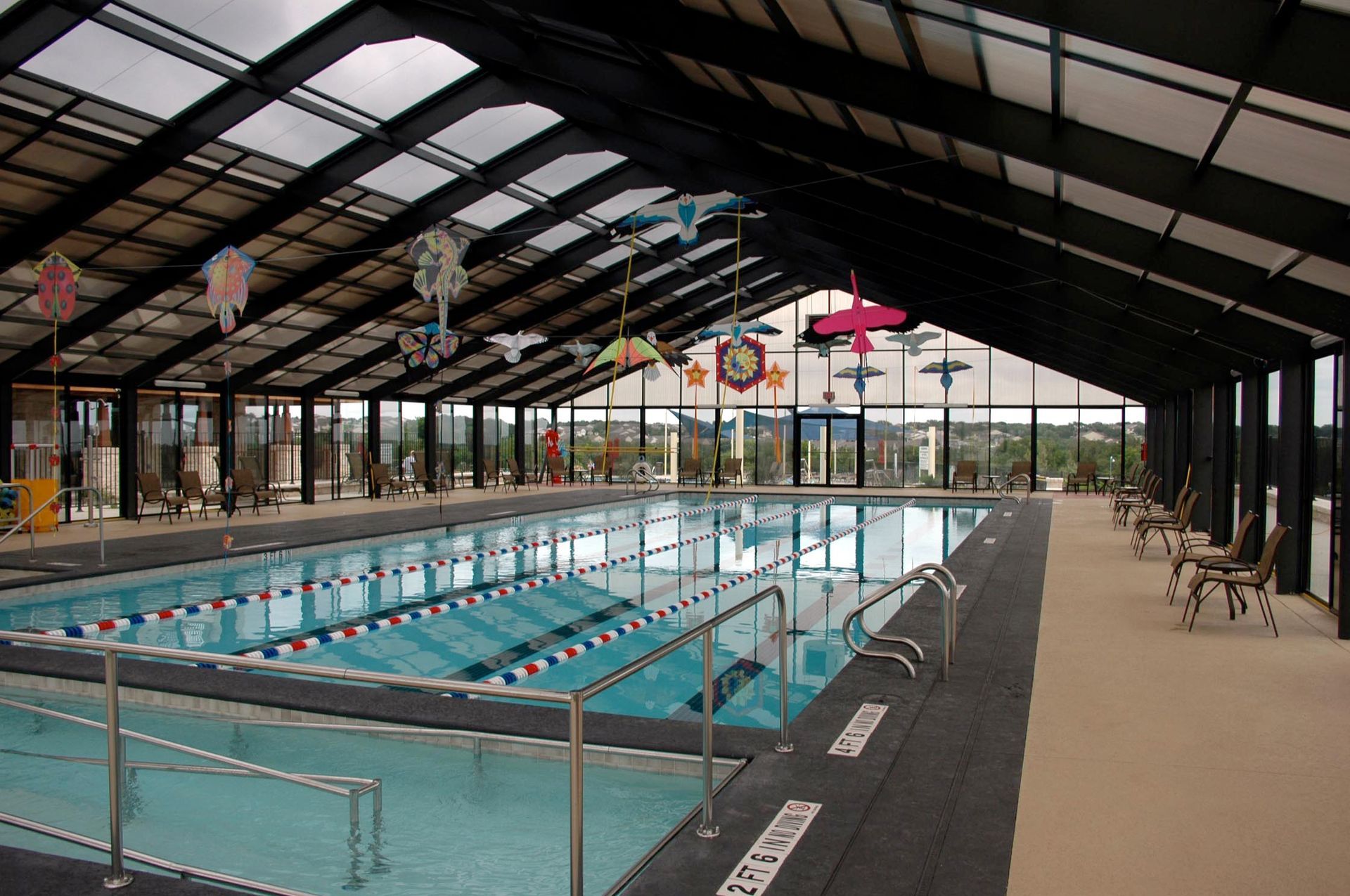 Indoor swimming pool with lane markers and a high arched roof, viewed from the deck