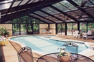 Indoor swimming pool under a glass roof with lounge chairs and tables around it