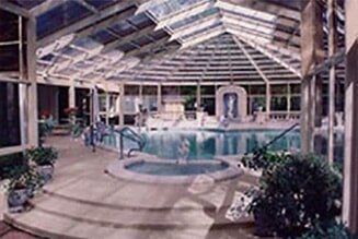 Indoor pool under a glass-roofed atrium with lounge chairs and plants