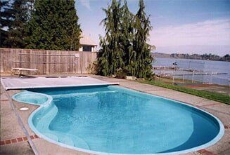 Curved backyard swimming pool beside a wooden fence with a lake view