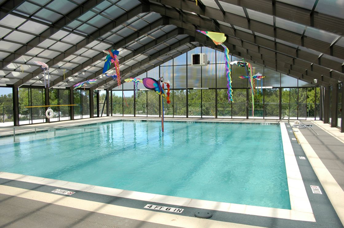 Indoor swimming pool with clear water, lane markings, and colorful flags under a metal roof