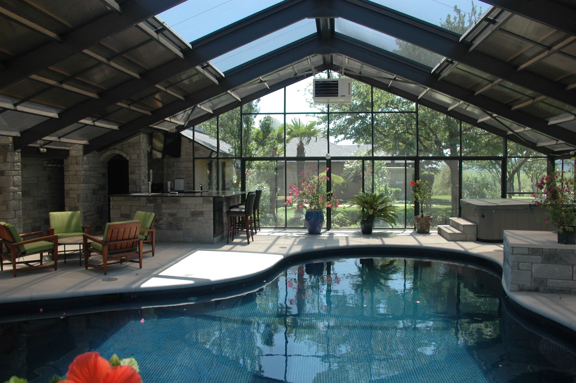 Indoor pool under a glass roof with stone walls, lounge chairs, and plants in a sunlit patio setting