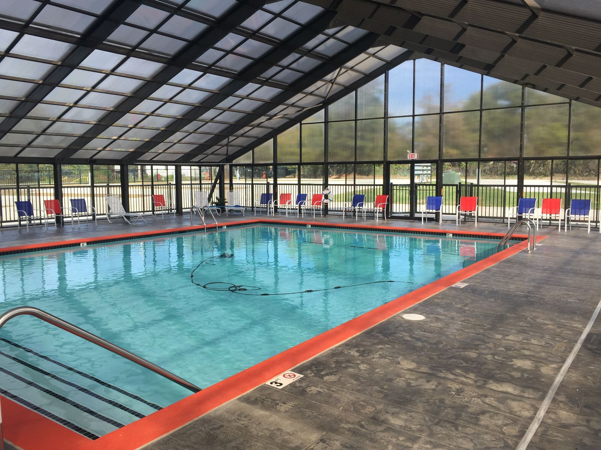 Indoor swimming pool with clear water, red deck edges, and large glass windows under a curved roof.