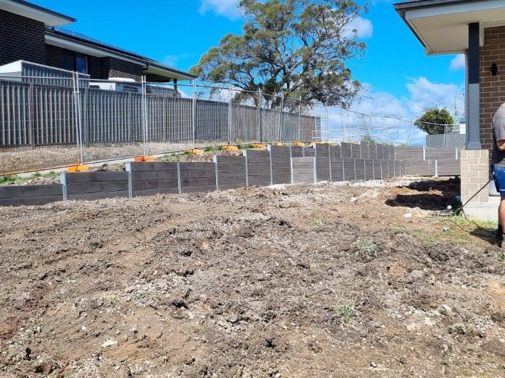 A Dirt Yard With a Retaining Wall in Front of Two Houses — Creating Eden Landscaping In Speers Point, NSW