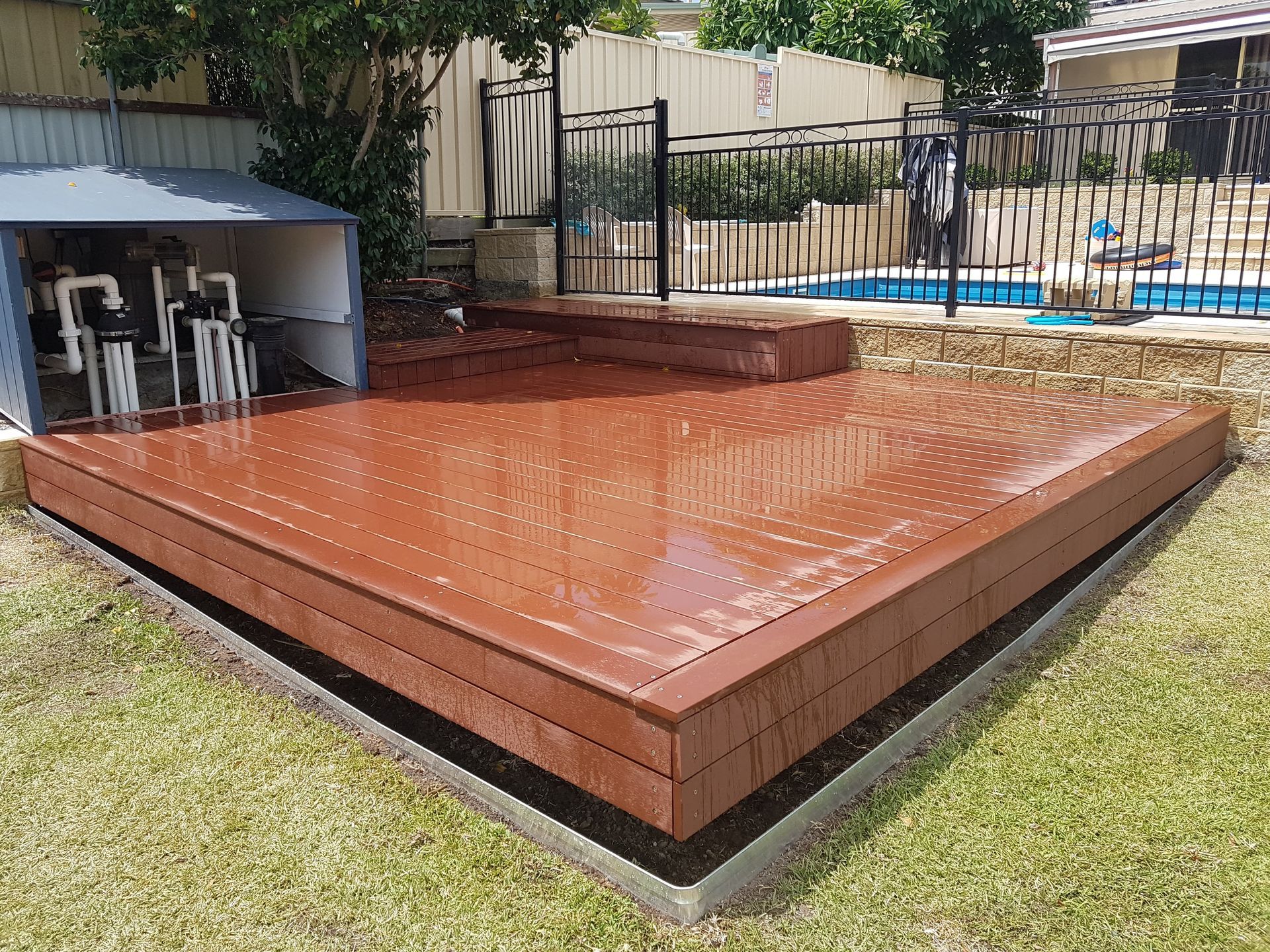 Wooden deck with pool in background, built on a raised concrete foundation with steps.