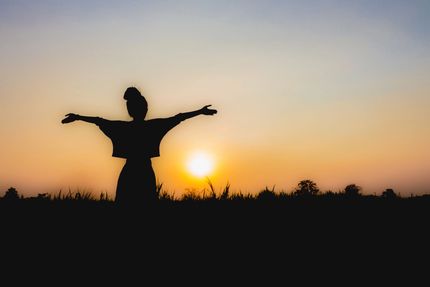 Silhouette di una persona con le braccia tese al tramonto in un campo aperto.