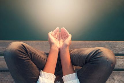Mani che reggono una piccola luce brillante sopra gambe incrociate su un pavimento di legno