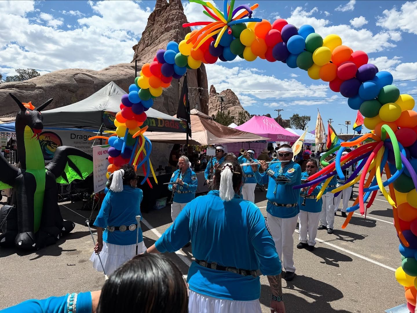 A group of people are standing under a rainbow colored balloon arch.