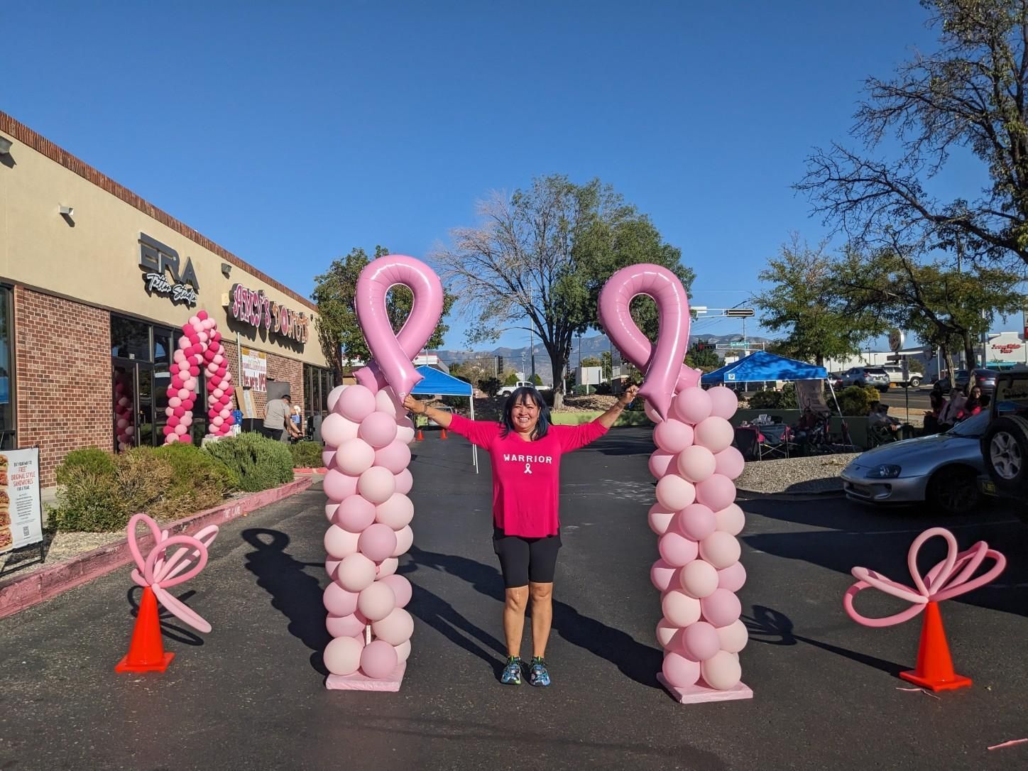 A woman in a pink shirt is standing in front of pink balloons