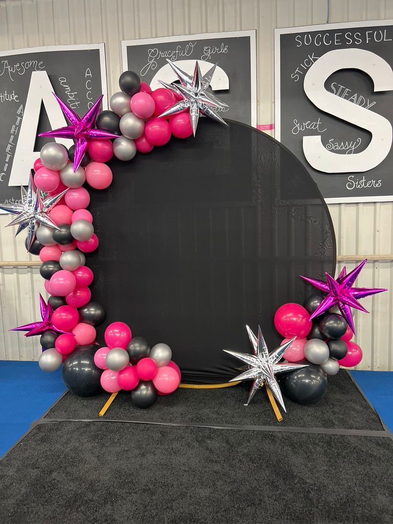 A black circle surrounded by pink , black , and silver balloons and stars.