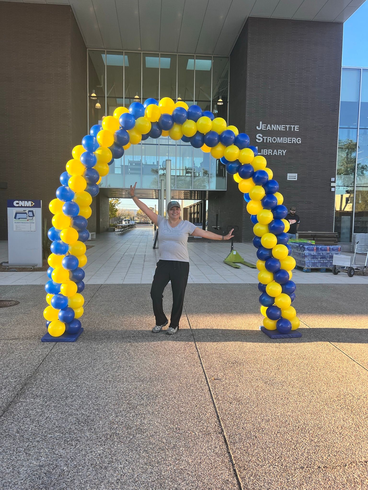 A man is standing under a yellow and blue balloon arch.