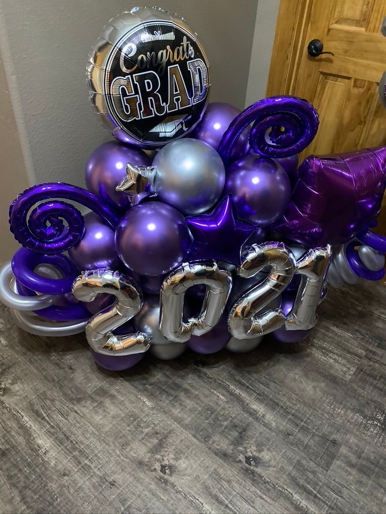 A bunch of purple and silver balloons are sitting on a wooden floor.