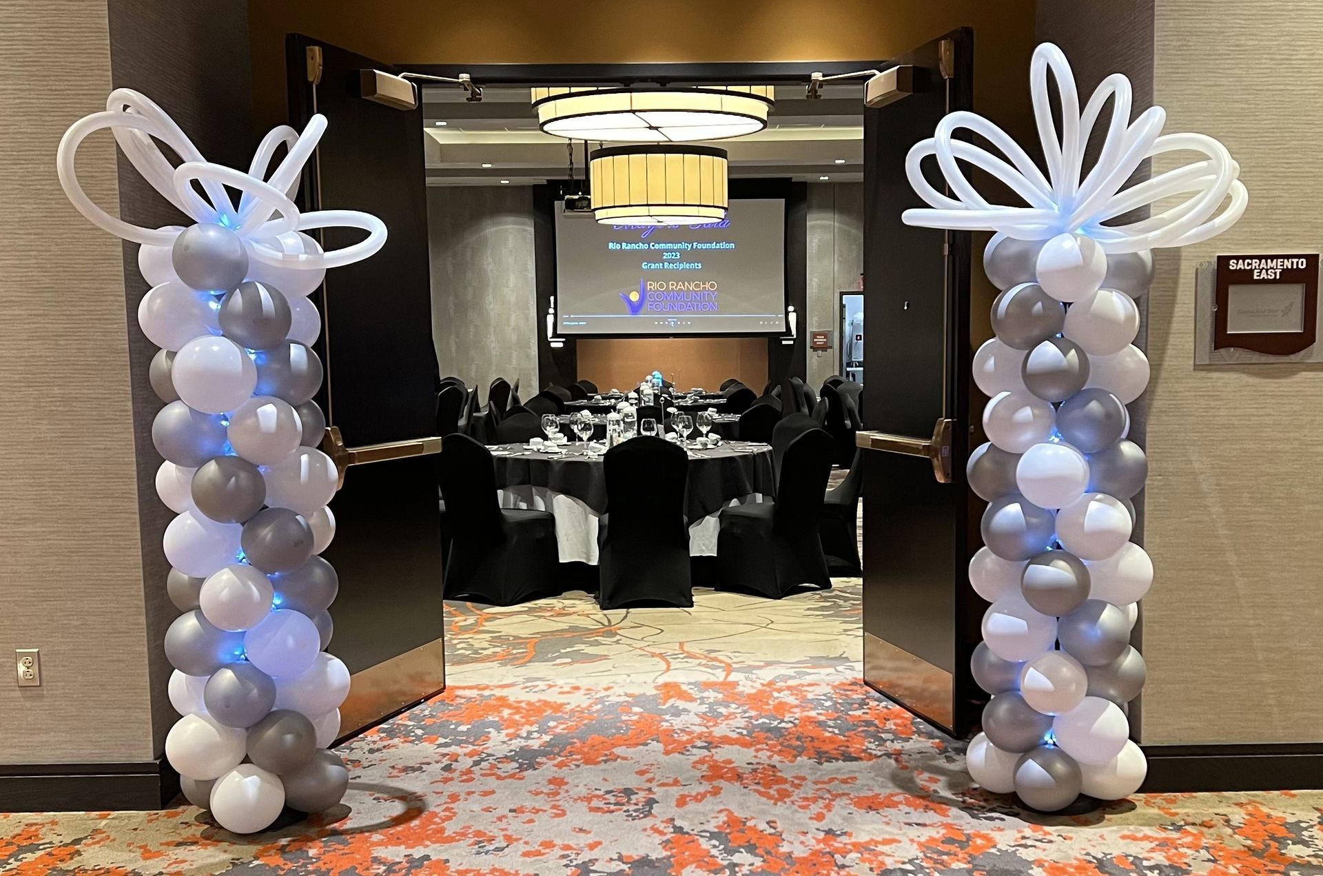A room with tables and chairs decorated with balloons and a projector screen.
