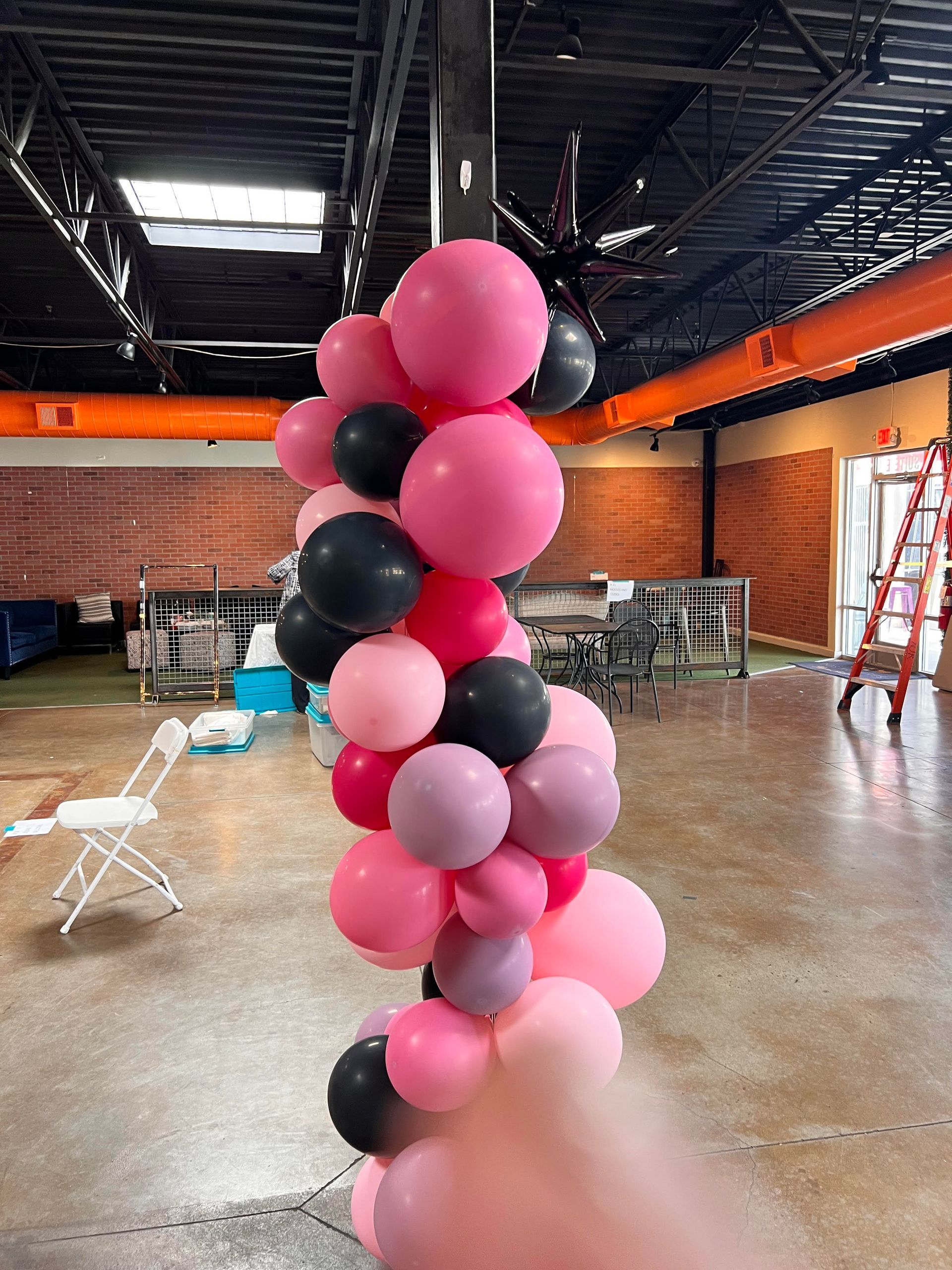 A bunch of pink and black balloons are stacked on top of each other in a room.