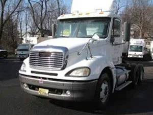 White semi-truck parked outdoors, with a chrome grill and black wheels. Other vehicles are in the background.