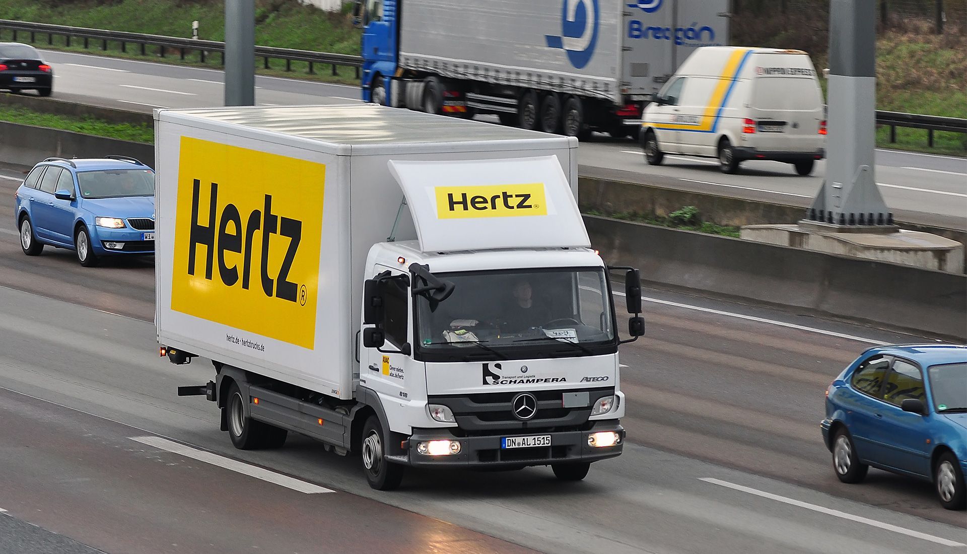 Hertz rental truck on a highway, with cars and other trucks. Yellow and white branding is visible.