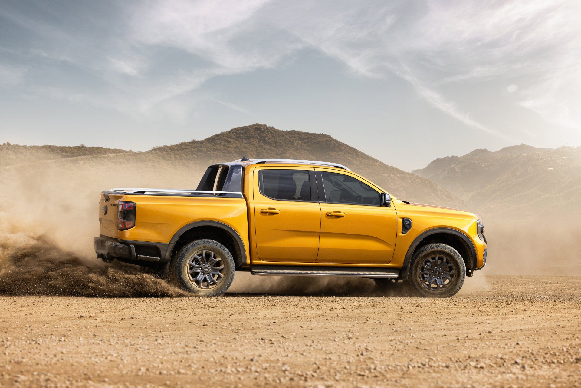 Yellow pickup truck driving on a dirt road, kicking up dust.