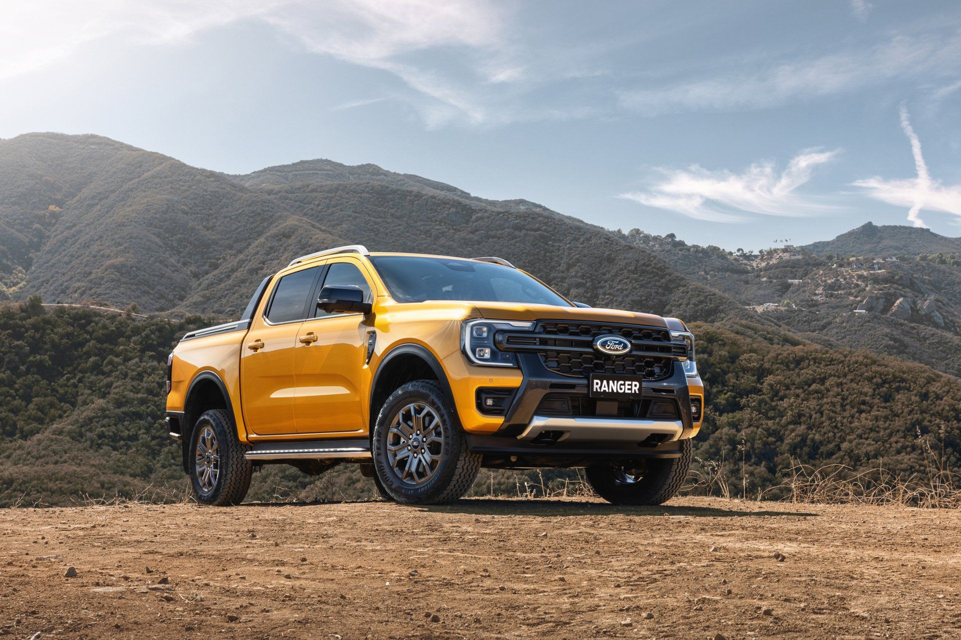 Yellow Ford Ranger truck on a dirt road, mountains in the background.