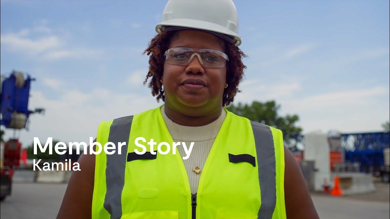 Woman in hard hat and safety vest smiles on a construction site.