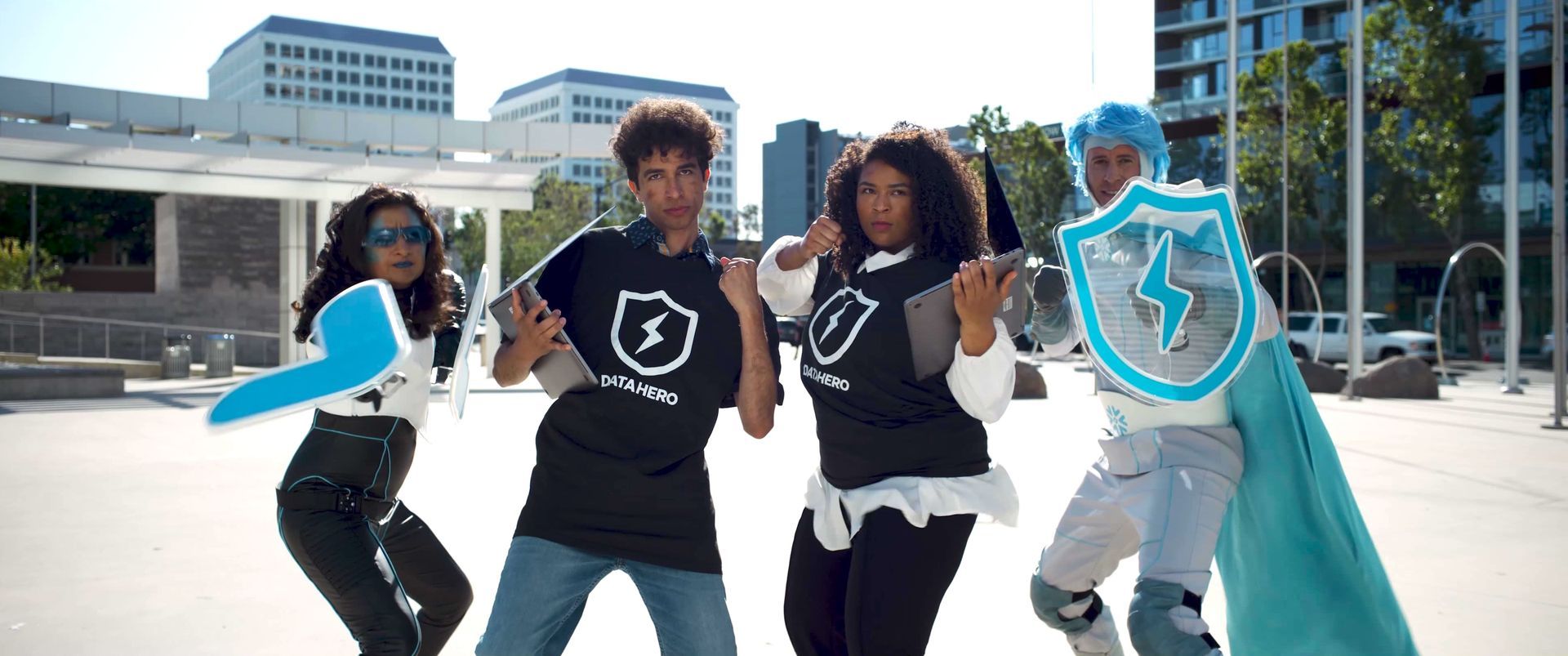 Four people in a city pose; one holds a shield. All wear the same logo: a lightning bolt inside a shield.