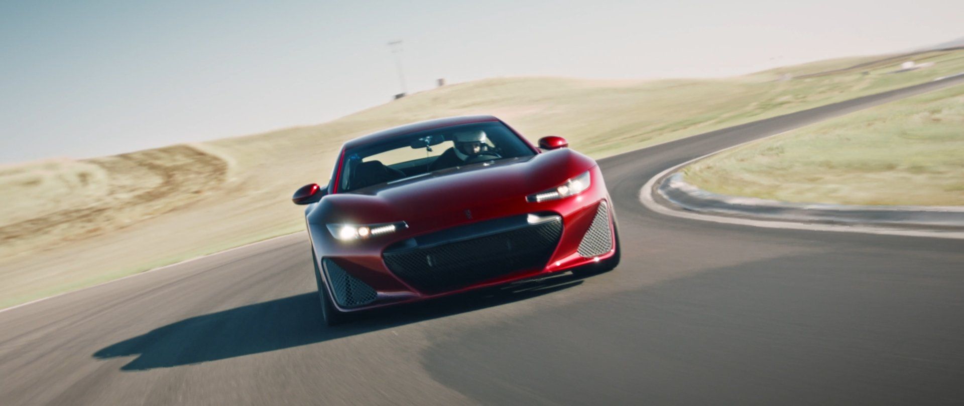 Red sports car speeds around a racetrack bend.