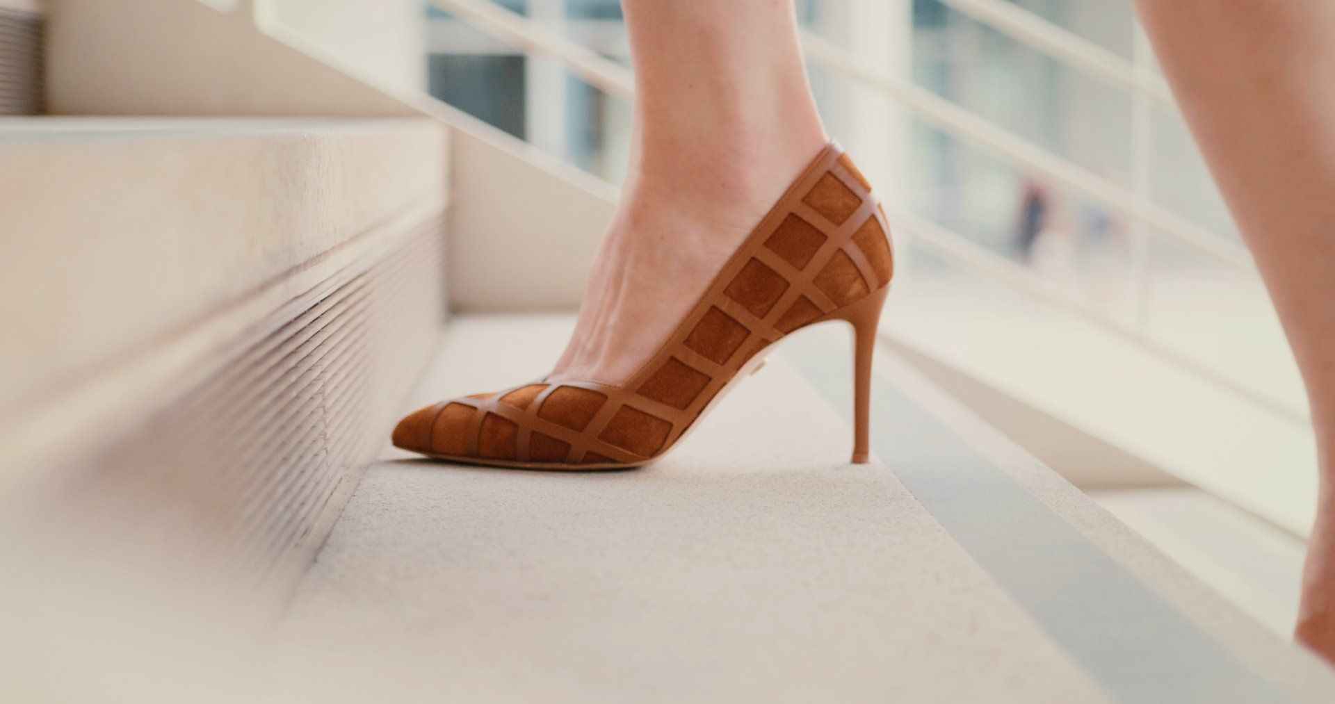 Brown high-heeled shoe stepping up a white staircase.