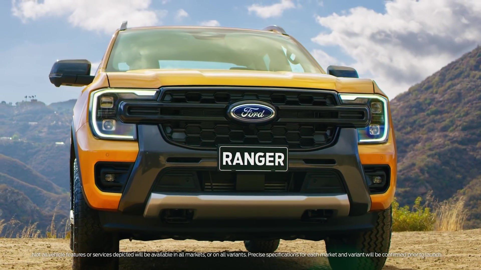 Orange Ford Ranger truck on a dirt road, facing the viewer with a mountain backdrop.