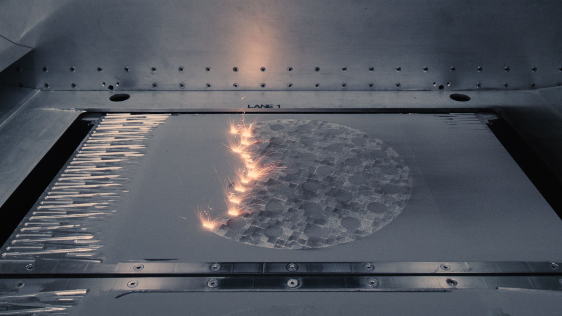 A machine welds a circular pattern onto a metal surface with sparks and heat.