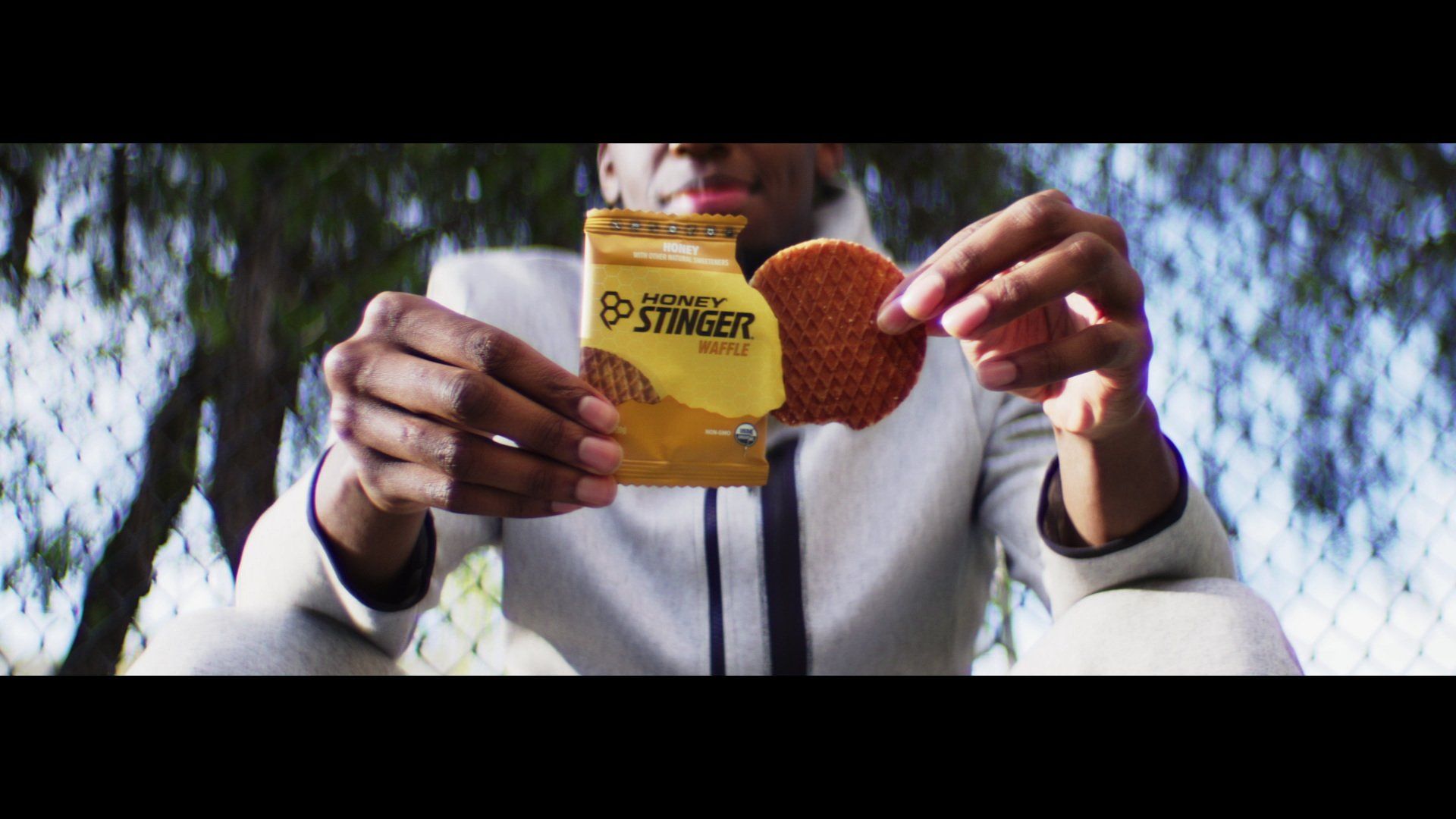 Person holding a package of Honey Stinger waffle and a waffle outdoors.