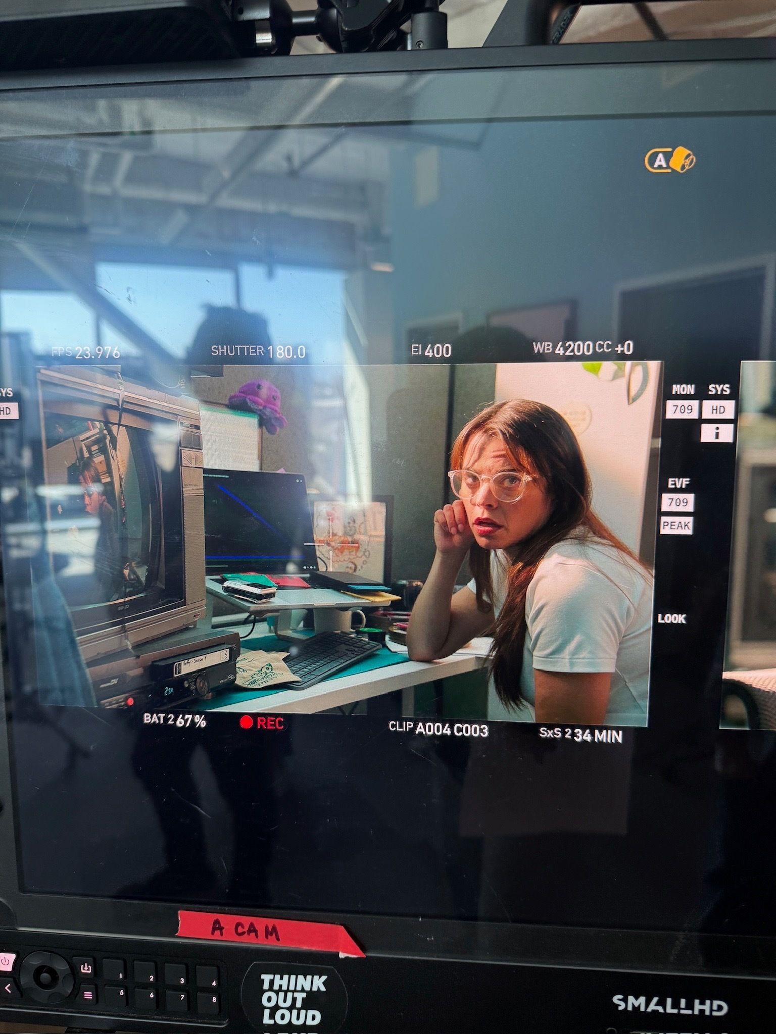 Person on a computer monitor in a dim room, hand on face, with game-like interface on screen