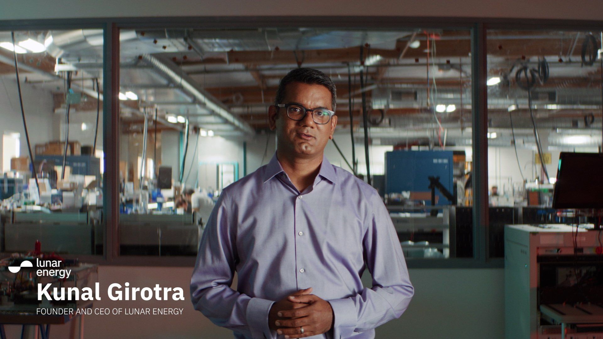 Man in glasses in a manufacturing facility. He stands in front of machinery and looks at the camera.