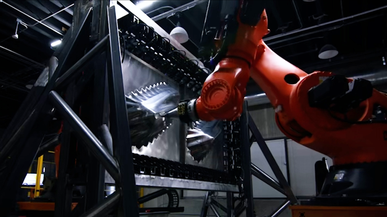 Orange robotic arm welding inside a metal frame. Black and silver metal parts. Factory setting.