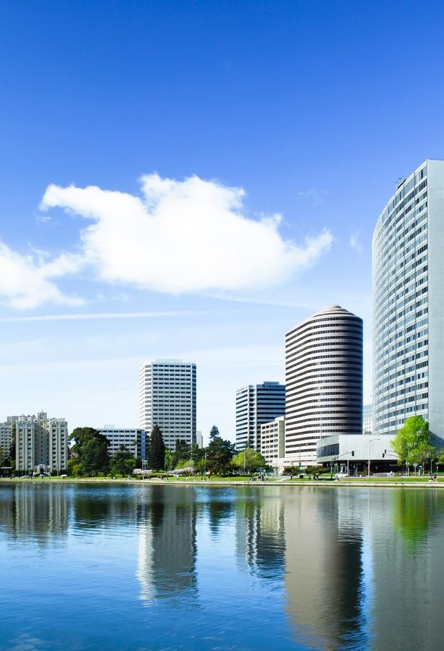 Modern waterfront skyline with tall glass buildings reflected in calm water under a blue sky