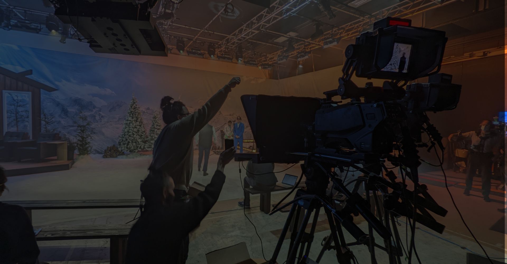 Silhouetted camera operator filming a studio stage with a seated performer under warm lights