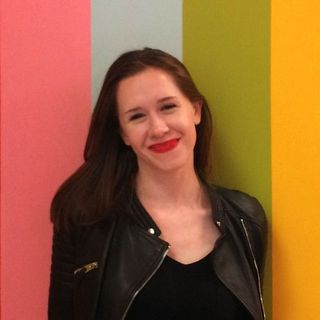 Woman wearing a black leather jacket and red lipstick smiles in front of a colorful wall.
